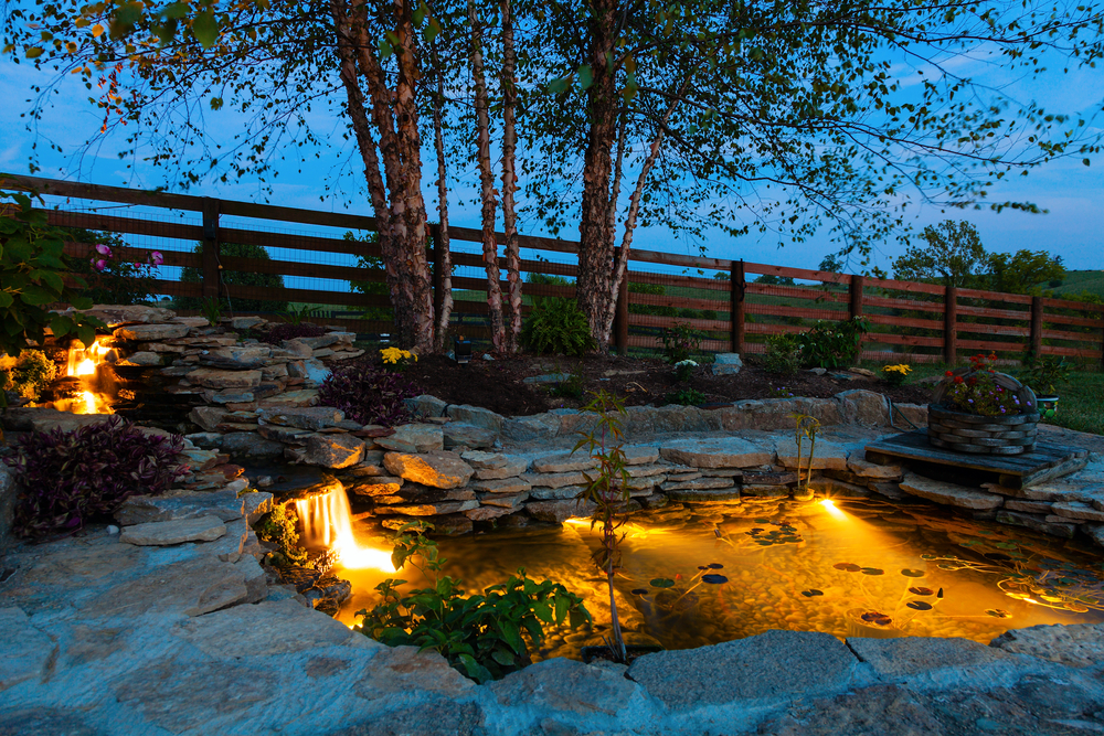 a backyard feature that is a lit-up pond with rocks for the edges
